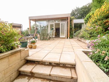 A tiled patio area with outdoor chairs and tables surrounded by plants and flowers at Under Catswood in Elcombe near Stroud