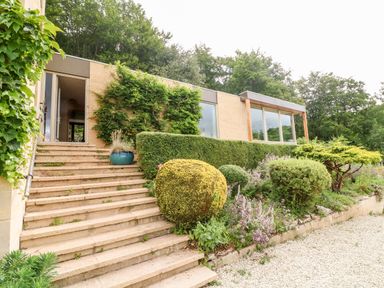 Outdoor stone steps leading to a modern house with a garden of trimmed bushes and plants at Under Catswood in Elcombe near Stroud