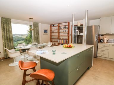 A kitchen with an island and bar stools and a dining table near a large window at Under Catswood in Elcombe near Stroud