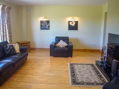 A living room with black leather sofas floral cushions wooden flooring and a fireplace at Tra Gheal in Kilmore County Wexford