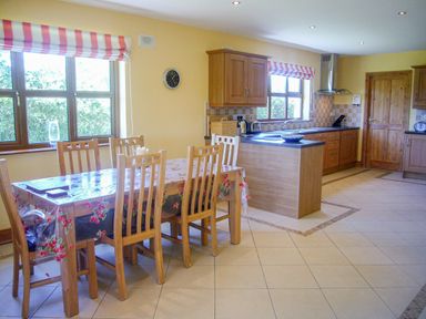 A kitchen with a dining table and wooden chairs near windows with striped blinds at Tra Gheal in Kilmore County Wexford