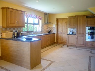 A kitchen with wooden cabinets tiled floor and a window with a striped blind at Tra Gheal in Kilmore County Wexford