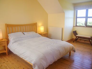 A bedroom with a wooden bed frame bedside tables with lamps a window and a bench at Tra Gheal in Kilmore County Wexford