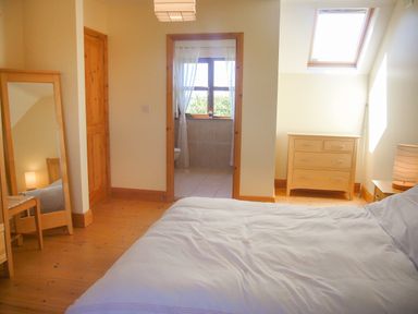 A bedroom with a bed a wooden dresser a mirror and a view into a bathroom at Tra Gheal in Kilmore County Wexford