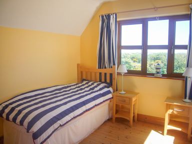 A bedroom with a single bed striped bedding two bedside tables with lamps and a window with curtains at Tra Gheal Kilmore County Wexford