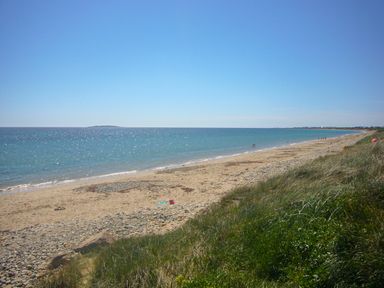 A sandy beach with pebbles and grass near the shore with people walking along the water at Tra Gheal in Kilmore County Wexford