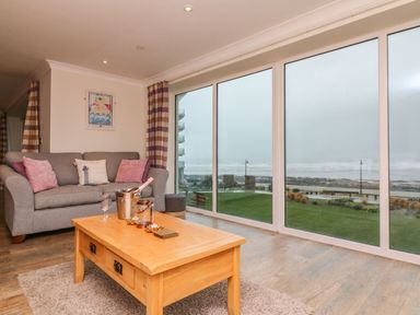 A living room with a gray sofa with pink cushions and a wooden coffee table next to large windows overlooking the sea at The Lobster Pot in Westward Ho