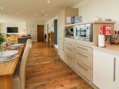A kitchen and dining area with wooden floor a dining table set with plates chairs and flowers cabinets with microwave oven at The Lobster Pot in Westward Ho
