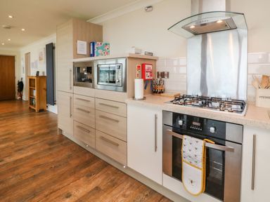 A kitchen with wooden cabinets a microwave oven stove with oven and utensils in a container on the counter at The Lobster Pot in Westward Ho