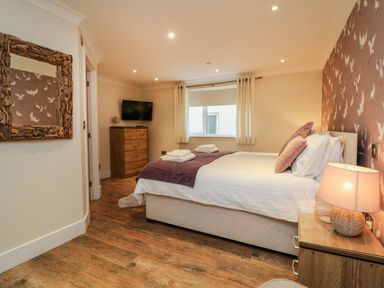 A bedroom with a bed, bedside table with lamp, dresser, wall mirror, and window at The Lobster Pot in Westward Ho