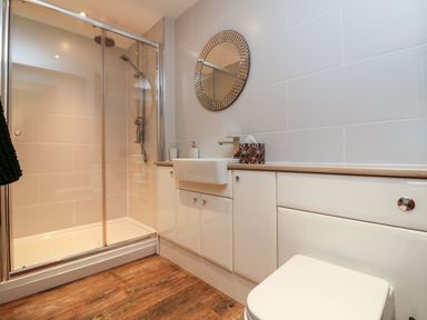 A bathroom with a shower enclosure a sink with cabinets a round mirror and a toilet at The Lobster Pot in Westward Ho