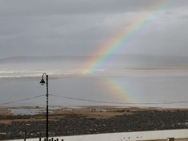 A beach with a rocky shore and a rainbow over the water with a lamppost in the foreground at The Lobster Pot in Westward Ho