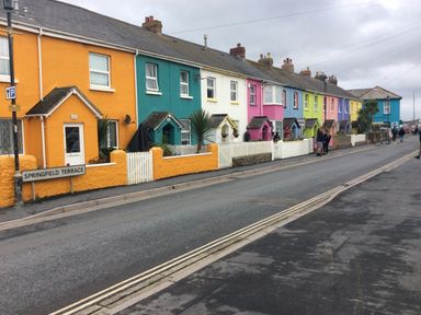 A row of colorful terraced houses along a street with some people walking at The Lobster Pot in Westward Ho