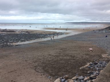 A sandy and rocky beach with people walking and playing near the water at The Lobster Pot in Westward Ho