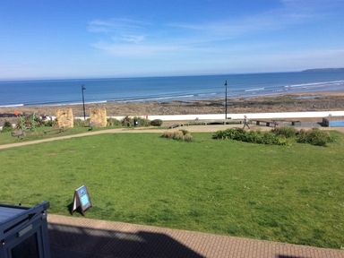 A grassy park area with benches and a walking path near a rocky beach and ocean at The Lobster Pot in Westward Ho