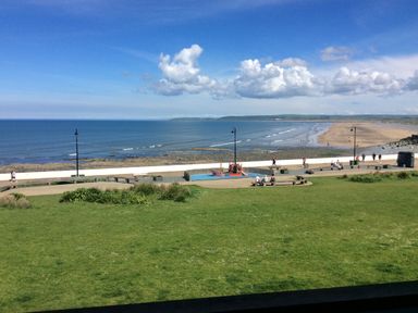A grassy area with a playground and a walkway along a beach with the sea and clouds at The Lobster Pot in Westward Ho