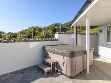 An outdoor hot tub with steps on a patio next to a white house at Haul A Gwynt in Criccieth