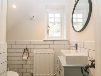 A small bathroom with a window radiator white tiles a round mirror and a sink at Haul A Gwynt in Criccieth