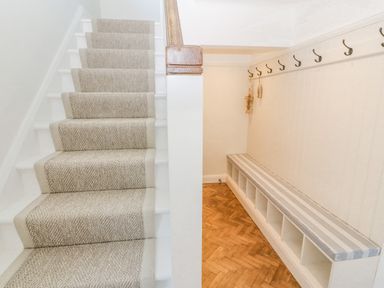 A staircase with a carpet runner next to a hallway with a bench and hooks on the wall at Haul A Gwynt in Criccieth