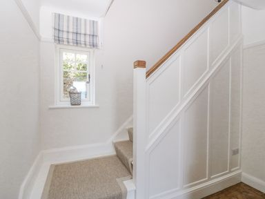 A staircase with carpeted steps next to a window with a striped roman blind and a basket on the window sill at Haul A Gwynt in Criccieth