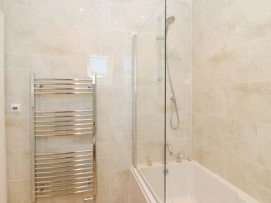 A bathroom with a bathtub shower combination and a metal towel radiator at Haul A Gwynt in Criccieth