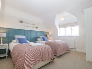 A bedroom with two single beds with red striped covers and blue pillows two nightstands with lamps and two decorative oars on the wall at Haul A Gwynt in Criccieth