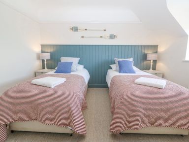 A bedroom with two single beds with striped bedspreads and pillows a blue panel behind the beds and two lamps on side tables at Haul A Gwynt in Criccieth
