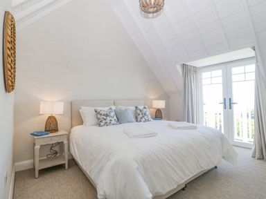 A bedroom with a large bed two bedside tables and lamps under a sloped ceiling at Haul A Gwynt in Criccieth