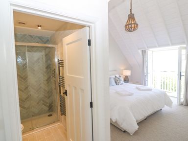 A bedroom with a bed and bedside lamp next to a bathroom with a tiled shower at Haul A Gwynt in Criccieth
