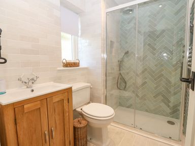 A bathroom with a wooden vanity unit a toilet a wicker basket and a shower with glass doors at Haul A Gwynt in Criccieth