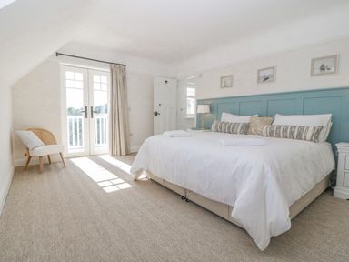 A bedroom with a large bed pillows lamps a chair and double doors leading outside at Haul A Gwynt in Criccieth
