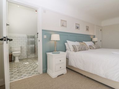 A bedroom with a double bed pillows bedside tables lamps and an open door leading to a bathroom at Haul A Gwynt in Criccieth