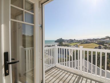 A balcony with white railing overlooking a coastal view with houses and a castle in the distance at Haul A Gwynt in Criccieth