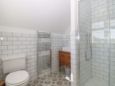 A bathroom with a toilet towel rack sink on wooden cabinet and a shower at Haul A Gwynt in Criccieth