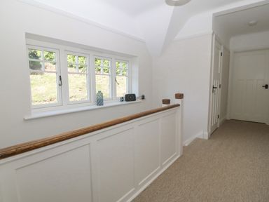 A hallway with beige carpet white paneled walls wooden handrail windows with objects on the sill and closed doors at Haul A Gwynt in Criccieth