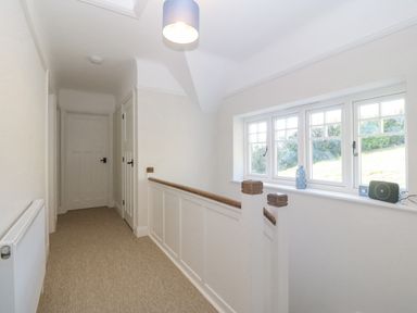 A hallway with carpeted floor radiator and windows with items on the windowsill at Haul A Gwynt in Criccieth