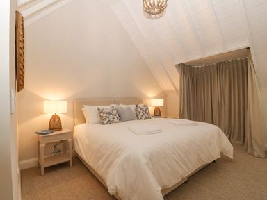 A bedroom with a large bed two bedside tables with lamps and a window with closed curtains at Haul A Gwynt in Criccieth