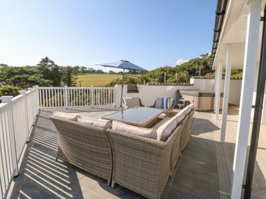 An outdoor patio with wicker seating furniture a glass table an umbrella and a hot tub on a terrace at Haul A Gwynt in Criccieth