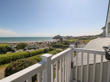 A balcony overlooking houses green hedges and a beach with a castle on a hill in the distance at Haul A Gwynt in Criccieth