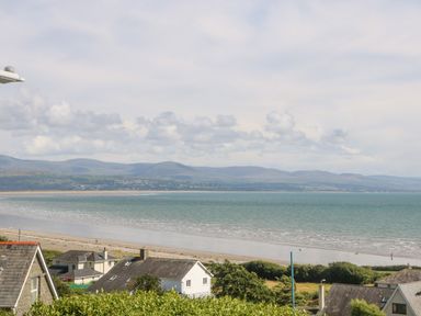 A coastal view with houses, a beach, sea, and mountains in the background at Haul A Gwynt in Criccieth