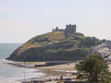 A coastal hill with castle ruins on top by the sea with houses and trees nearby at Haul A Gwynt in Criccieth