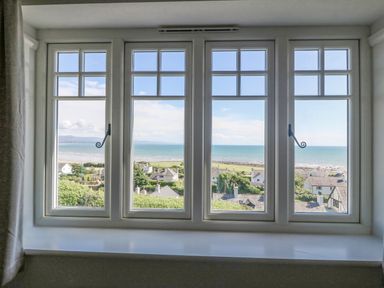A large four-panel window overlooking houses greenery and a coastline at Haul A Gwynt in Criccieth