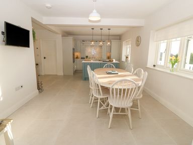 A dining area with a wooden table and white chairs next to windows in a kitchen at Haul A Gwynt in Criccieth