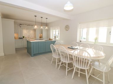 A kitchen and dining area with a wooden dining table and white chairs near windows at Haul A Gwynt in Criccieth