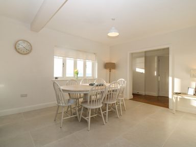 A dining room with a round table and eight chairs near a window with flowers at Haul A Gwynt in Criccieth