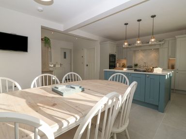 A kitchen with a dining table and six chairs a kitchen island with pendant lights and cabinets at Haul A Gwynt in Criccieth