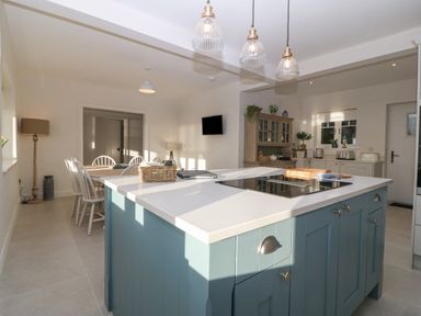 A kitchen with a blue island unit and dining table with white chairs at Haul A Gwynt in Criccieth