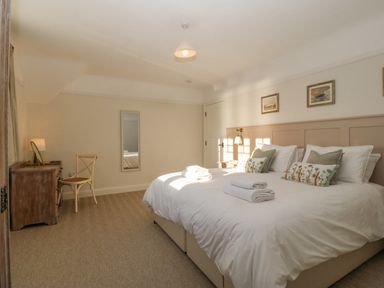 A bedroom with a double bed with pillows and towels bedside tables a chair a dresser and a mirror at Haul A Gwynt in Criccieth