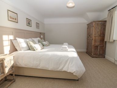 A bedroom with a large bed with pillows and folded towels alongside a wooden wardrobe and bedside table at Haul A Gwynt in Criccieth