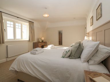 A bedroom with a double bed with white linens and pillows a wooden desk with a chair and lamp a mirror on the wall and windows with curtains at Haul A Gwynt in Criccieth